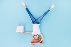 Top above high angle view full size photo of foolish carefree girl kid ride skate upsidedown deliver gift box show tongue wear white t-shirt denim jeans lay isolated over blue color background
