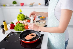 Cropped photo of housewife lady hands put fresh raw salmon fillet steak lying flying pan adding spices salty cooking family dinner wear apron t-shirt stand modern kitchen indoors