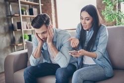 Photo of two people frustrated woman use smartphone search sms find another woman message point hand shocked man sit comfort cozy couch tired depressed in house indoors