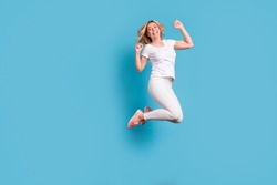 Full body photo of attractive funny crazy lady jump high up celebrating holiday raise fists astonished excited wear casual white s-shirt pants footwear isolated blue color background