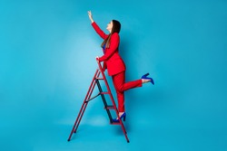Full length profile photo of professional fancy lady worker come up career ladder touch success with arm wear luxury red suit blazer pants high-heels isolated blue color background