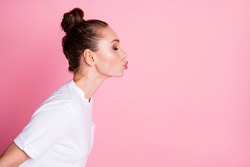Profile photo of attractive lady funny bun hairdo sending air kisses side empty space coquettish lovely girlish person eyes closed wear white t-shirt isolated pastel pink color background