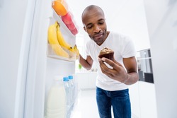Portrait of his he nice attractive hungry guy looking in fridge taking unhealthy junk fat cupcake cake break pause regime in light white interior house kitchen indoors