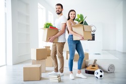 Full length body size view of  couple holding in hands stuff package settling down at place space flat light white interior house indoors