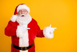 Photo astonished beard santa claus impressed x-mas  christmas adverts discount point finger copyspace wear cap headwear stylish trendy costume isolated bright shine color background
