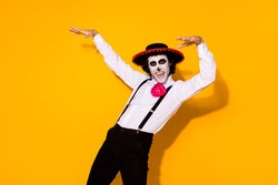 Photo of scary zombie creature guy jump scare raise pretend hands tree branches horror movie casting wear white shirt death costume sugar skull suspenders isolated yellow color background