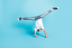 Small kid stand hands do acrobatic trick wear white shirt jeans sneakers isolated blue color background