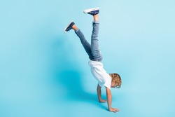 Full length photo of little kid stand hands raise legs wear white shirt jeans sneakers isolated blue color background