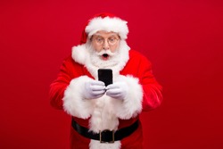 Portrait of his he nice attractive handsome amazed stunned Santa using gadget 5g fast speed blog blogger browsing multimedia isolated over bright vivid shine vibrant red color background