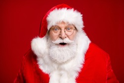 Photo of retired old man grey beard open mouth excited look see magical newyear creature make wish bring atmosphere wear santa costume coat spectacles headwear isolated red color background