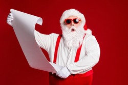 Portrait of his he attractive amazed fat white-haired Santa holding in hands reading wish present gift list pout lips order isolated bright vivid shine vibrant red burgundy maroon color background