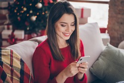 Photo of positive girl typing letter on smartphone sit comfort couch in house indoors with x-mas christmas ornament