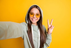 Photo of beautiful brunette hair kid show arm finger v-sign on selfie hoodie isolated on yellow color background