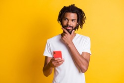 Photo of tricky influencer dark skin guy hold telephone look side sly eyes wear t-shirt isolated yellow color background