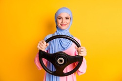 Portrait of content pretty cheery muslimah wearing hijab driving invisible car leasing isolated on bright yellow color background