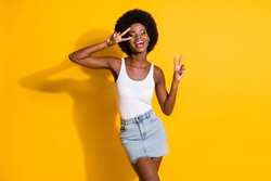Portrait of lovely cheerful wavy-haired lady showing v-sign having fun dancing isolated over bright yellow color background