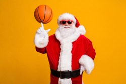 Portrait of his he nice attractive cheerful cheery Santa spinning of forefinger finger orange ball workout activity hobby isolated over bright vivid shine vibrant yellow color background