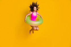 Photo portrait of young curly girl jumping into pool holding breath closed eyes with inflatable green circle wearing fuchsia swim wear isolated on vivid yellow colored background