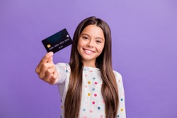 Photo portrait of smiling little girl with long brunette hair showing blurred debit card isolated on bright purple color background