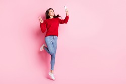 Full length photo of pretty girl jump hold telephone make selfie show v-sign wear red sweater jeans sneakers isolated pink color background