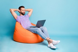 Full length body size photo of bearded programmer chilling during break in orange beanbag isolated on vivid blue color background