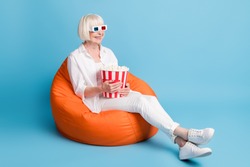 Full length body size photo of senior woman in cinema keeping pop corn box watching movie isolated on bright blue color background