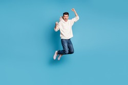 Full size photo of young happy positive good mood man jumping screaming raise fists in victory isolated on blue color background