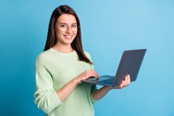 Photo of positive girl working on laptop wear green sweater isolated over blue color background