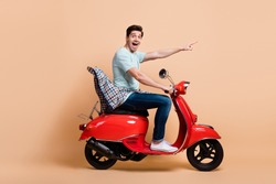Profile side view portrait of nice amazed cheerful guy driving moped pointing far away way road isolated over beige pastel color background
