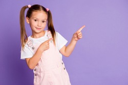 Photo of charming little girl point index finger empty space wear pink dress isolated on purple color background
