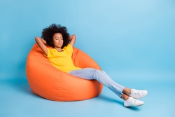 Full size photo of dark skin little brown haired girl sit sleep bean bag isolated on blue color background