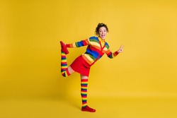 Photo of attractive crazy lady showing v-sign stretch one leg wear striped pullover short skirt knee socks shoes isolated yellow color background