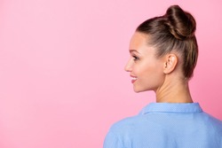 Back view photo portrait of girl bun hairstyle looking at blank space smiling in blue dotted shirt isolated on pastel pink color background