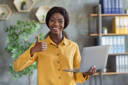 Photo portrait of african american woman holding laptop showing thumb up in modern office indoors