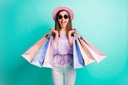 Photo of optimistic brunette girl hold bags open mouth wear purple shirt cap trousers spectacles isolated on blue color background