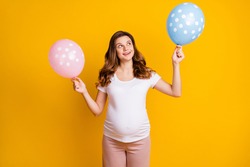 Portrait of pretty cheerful dreamy pregnant girl holding in hands dotted air balls twins isolated over bright yellow color background