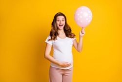 Portrait of lovely amazed cheery pregnant girl holding in hand air ball childbirth isolated over bright yellow color background