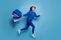 Full body profile photo of excited carefree person running hand hold bags open mouth isolated on blue color background