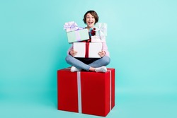 Photo of pretty adorable woman wear violet sweater sitting red gift holding stack presents space isolated turquoise color background