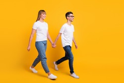 Full length photo of pretty adorable persons dressed t-shirt walking holding hands arms empty space isolated yellow color background