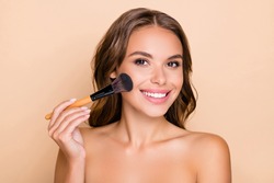 Photo of young happy smiling beautiful woman doing contouring apply blush on cheeks isolated on beige color background