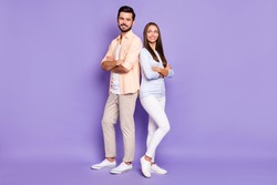 Full size portrait of two cheerful persons standing back to back folded arms isolated on purple color background