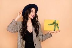 Photo portrait of excited girl holding small yellow present box isolated on pastel beige colored background