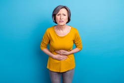 Portrait of attractive sick middle-aged woman feeling bad touching abdominal isolated over vivid blue color background