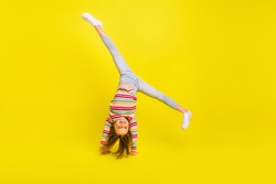 Full length photo of happy flexible little girl enjoy active weekend upside down isolated on yellow color background