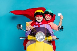 Portrait of two cheerful elderly retired pensioners riding moped using card buy order isolated over bright blue color background