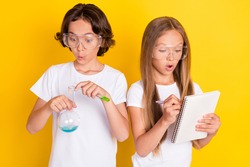 Portrait of two attractive amazed kids learning chemistry lab subject writing note isolated over bright yellow color background