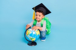 Portrait of nice cheerful boy wearing academic master cap holding globe isolated over bright blue color background