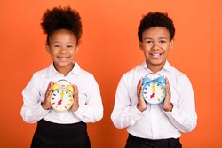 Photo of two young black kids happy positive smile hold clock timer watch education isolated over orange color background