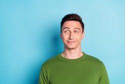 Photo of positive minded man look empty space think thoughts wear green pullover isolated blue color background